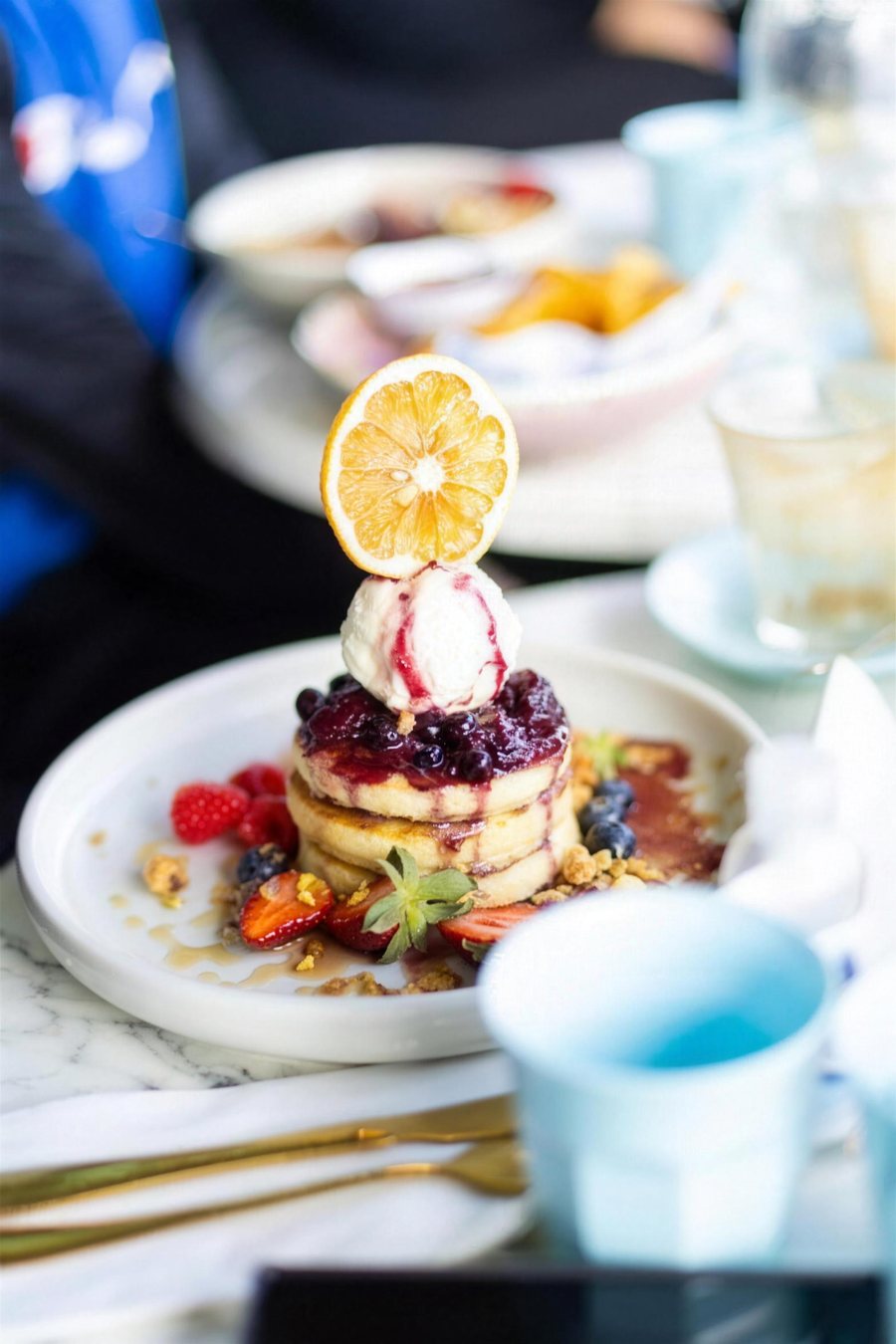 A stack of pancakes with berries and a dried orange slice on a white plate