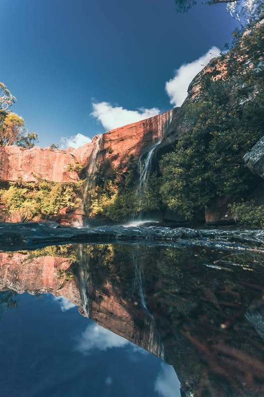 Red cliffs reflected in a still river under a blue sky