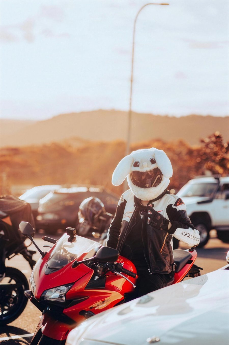 A rider in a white helmet with bunny ears sitting on a red sports motorbike