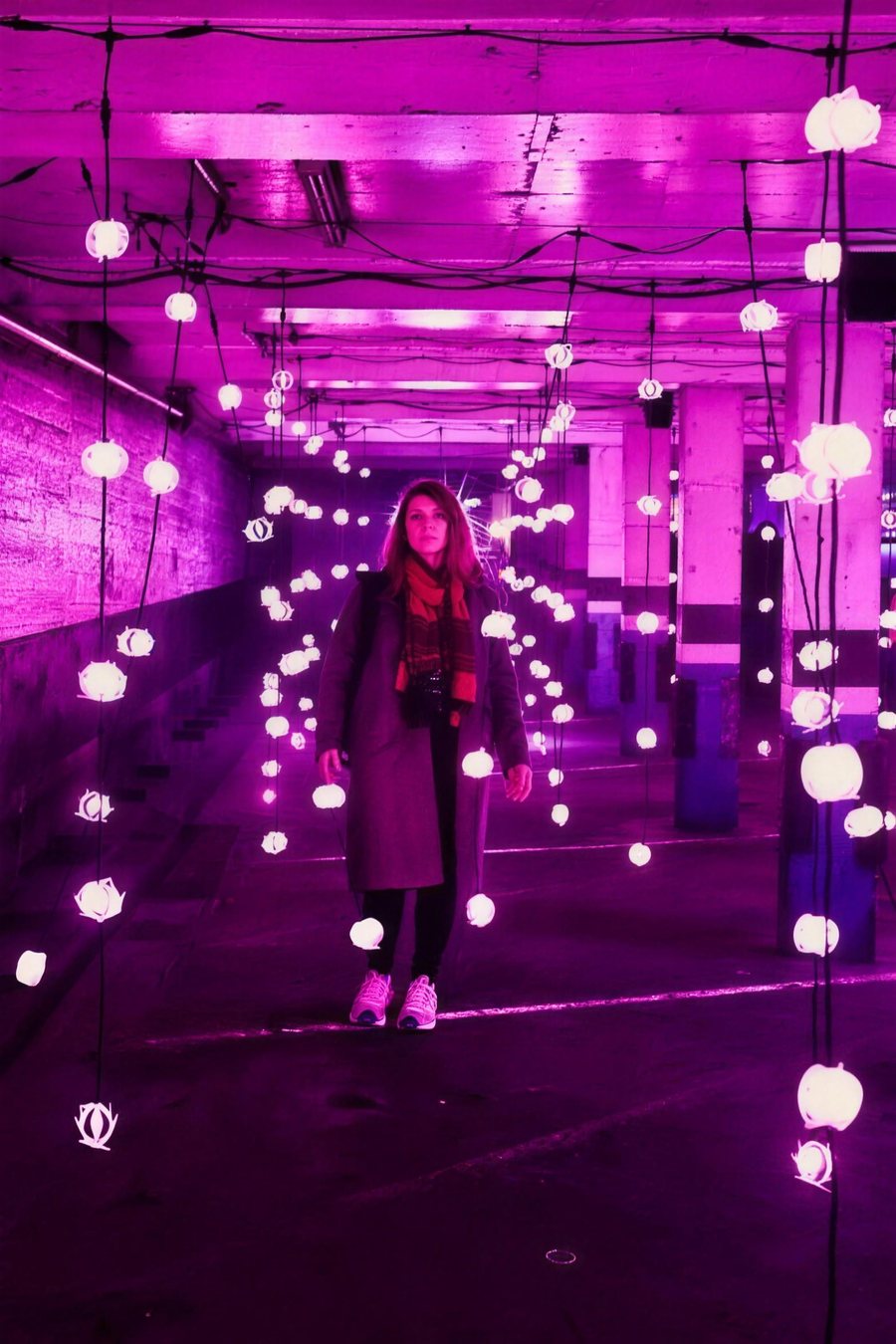 A woman standing among hanging lanterns in a purple lit hall